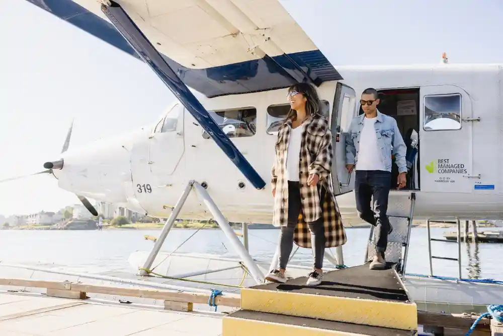 Two passengers stepping down from a floatplane onto the dock