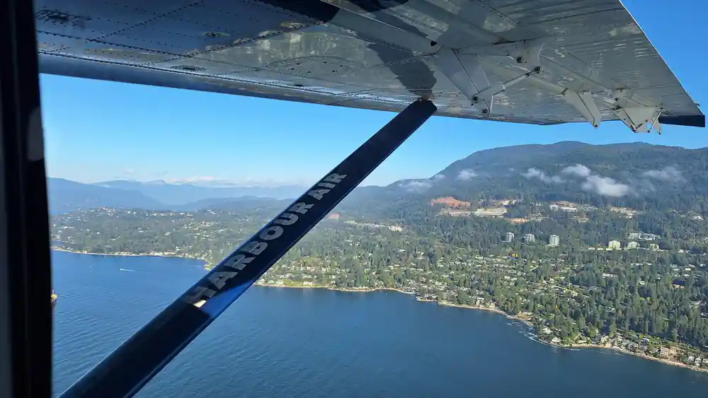 A wing strut and Harbour Air lettering over a forested shore